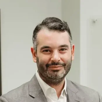 A man with short dark hair and a beard smiles slightly, exuding confidence in his light-colored suit jacket over a white shirt. The neutral, blurred indoor setting hints at Nguyen & Company, where his expertise as a CPA is both renowned and respected.