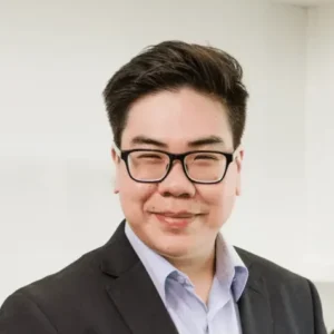 CPA with short dark hair and glasses, wearing a suit and light-colored shirt, smiling at the camera against a plain background, represents Nguyen & Company.